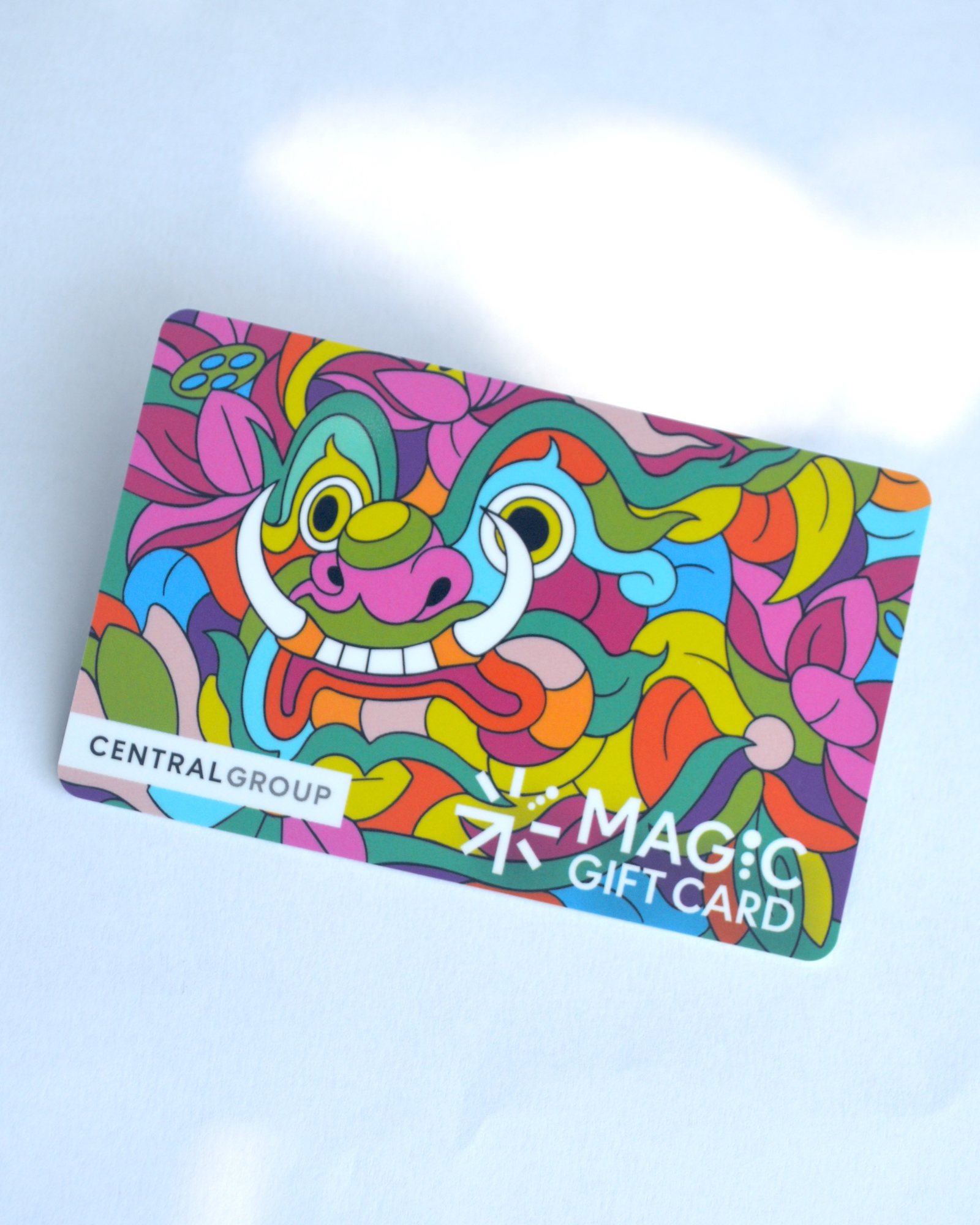 บัตรลายหลากสีวางเอียงบนพื้นสีอ่อน แสดงใบหน้าตาโต เขี้ยวขาวสองข้าง และดอกไม้ พร้อมข้อความ CENTRALGROUP และ MAGIC GIFT CARD